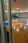An open door labeled "Fitness Room 2" reveals an empty gym studio with wood flooring, mirrors, and exercise bikes in the background.
