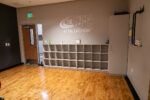 A room with cubby storage units against a wall labeled "The Rec at the Lakefront," a wooden door, hardwood floors, and a cabinet in the corner.