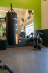 A gym with a heavy punching bag, weight plates on a rack, and a large mirror reflecting workout equipment and exercise space.