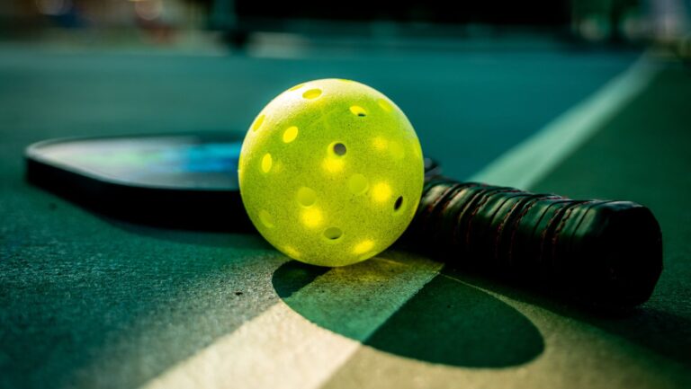 A yellow pickleball and a paddle rest on the indoor pickleball court at The Rec at The Lakefront, near a crisp white line.