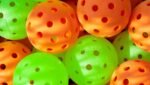 A close-up view of several green and orange plastic balls with holes, often used for indoor pickleball or wiffle ball, perfect for fitness fun at The Rec.